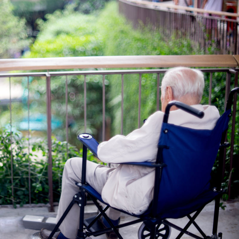 Old man in wheelchair sitting alone staring out at garden.