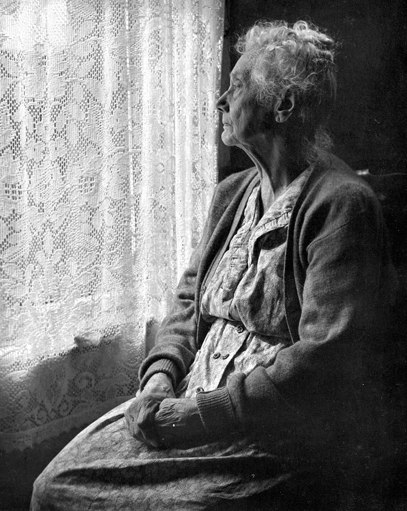 Older woman staring out window.